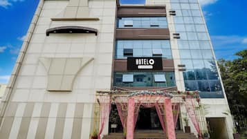 A modern hotel building with a prominent 'HOTEL' sign, a glass facade, and a decorative entrance with potted plants.