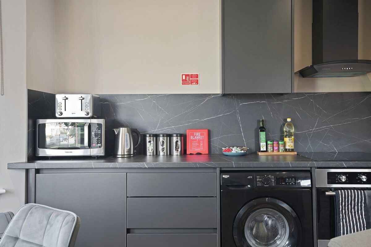 A compact kitchen with a microwave, toaster, kettle, and a dish rack.