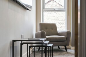 A corner room with a window, a grey armchair, and a small table. - The Olive Tree | Superior 2-Bed Apartment (Kingston upon Hull)