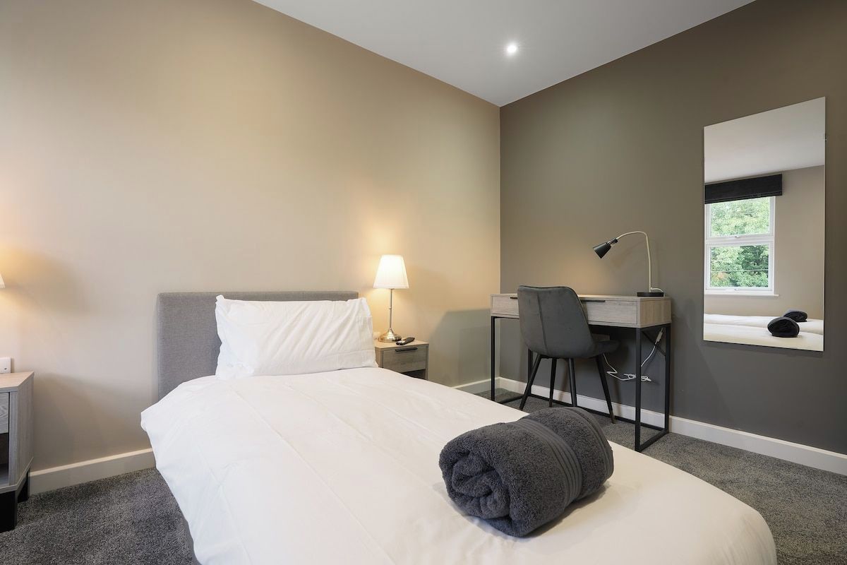 A hotel room with a bed, desk, chair, lamp, and a window.