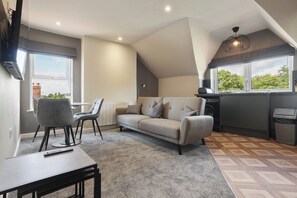 A modern living room with a sofa, chairs, a dining table, and a kitchen area with a window. - The Olive Tree | Stylish 2-Bed Loft (Kingston upon Hull)