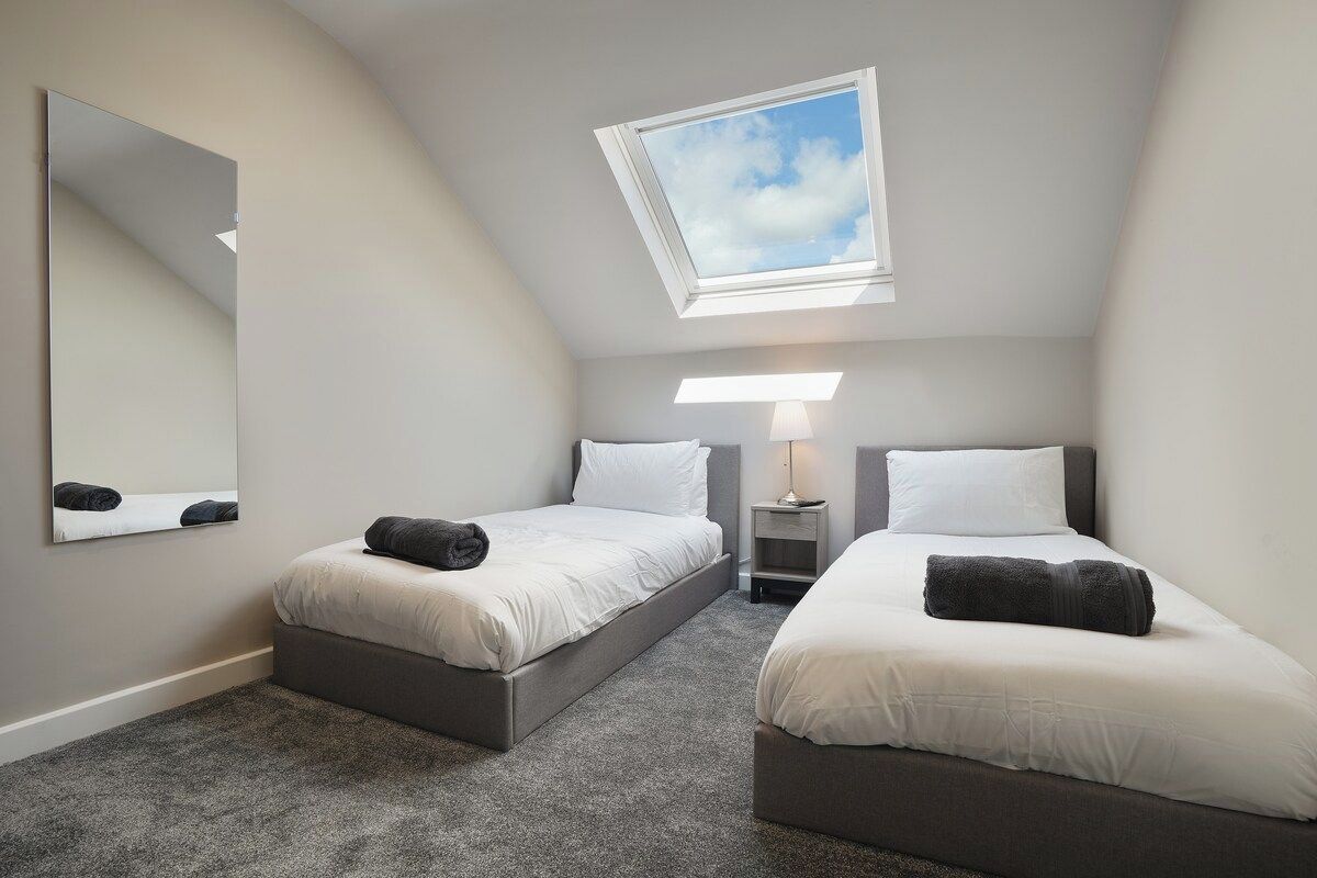 A bedroom with two beds, a skylight, a mirror, and bedside lamps.