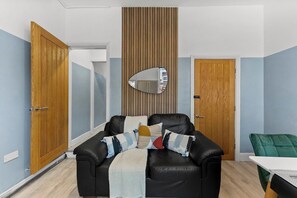 Una habitación con un sofá de cuero negro, una puerta de madera, un espejo y una silla verde.