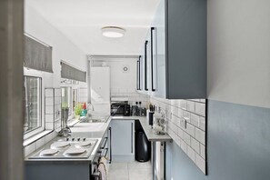 Una cocina moderna con baldosas blancas, electrodomésticos de acero inoxidable y un ventanal con persianas.