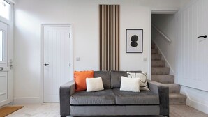 Un salón en tonos neutros con un sofá gris, una alfombra estampada, un panel de listones de madera verticales y un cuadro en la pared.