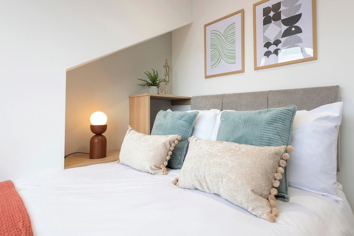 A bedroom with a bed, pillows, a bedside table with a lamp, and wall art.