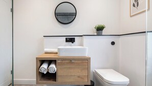 Un baño con un lavabo blanco, un inodoro, un tocador de madera con un espejo y una planta pequeña en la encimera.