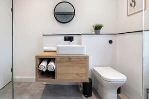 Ein Badezimmer mit einem weißen Waschbecken, einer Toilette, einer Holzkommode mit Spiegel und einer kleinen Pflanze auf der Ablagefläche.