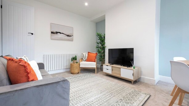 Una sala de estar moderna con un sofá, un televisor, un comedor y una planta.