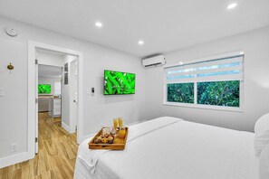 Ein Hotelzimmer mit Bett, Frühstückswagen, Fernseher, Klimaanlage und einem Fenster mit Blick auf Grünflächen.