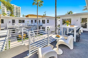 Eine Dachterrasse mit weißen Geländern, Sitzgelegenheiten im Freien und einem Esstisch mit einer Schüssel Essen.