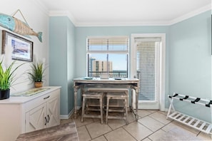 A room with a dining table, chairs, a window with blinds, a potted plant, and a framed picture on the wall. - Bluewater Resort 920-Oceanfront I/O Pool-Hot tub (Myrtle Beach)