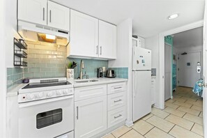 A kitchen with white cabinets, a stove, a sink, and a refrigerator. - Bluewater Resort 920-Oceanfront I/O Pool-Hot tub (Myrtle Beach)