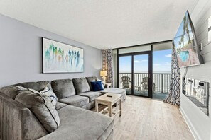 A modern living room with a grey sofa, a small wooden table, and a painting on the wall. - Compass Cove Mariner 1020- 3BR Great Amenities (Myrtle Beach)