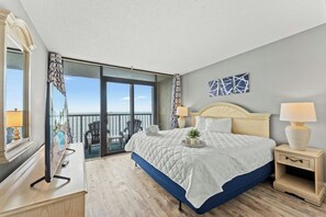 A hotel room with a large bed, a desk, a chair, and a balcony with a view. - Compass Cove Mariner 1020- 3BR Great Amenities (Myrtle Beach)
