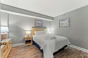 A bedroom with a bed, bedside tables, a lamp, and two framed pictures on the wall. - Compass Cove Mariner 1020- 3BR Great Amenities (Myrtle Beach)
