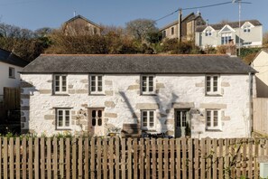 A stone building with multiple windows and a wooden fence in front. - Rose Cottage (Helston)
