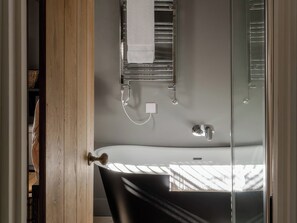 A bathroom with a bathtub, a towel hanging on a rack, and a window with a view of a bridge. - Rose Cottage (Helston)