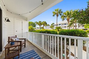 Uma varanda com mesa e cadeiras de madeira, um tapete azul e um corrimão branco.