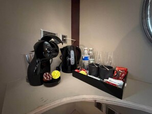 Ein Hotelzimmer mit Minibar, inklusive Kaffeemaschine, Wasserflasche, Gläsern und verschiedenen Snacks.