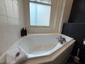 Ein Badezimmer mit einer freistehenden Badewanne, einem Fenster darüber und einer Toilette zur rechten Seite.