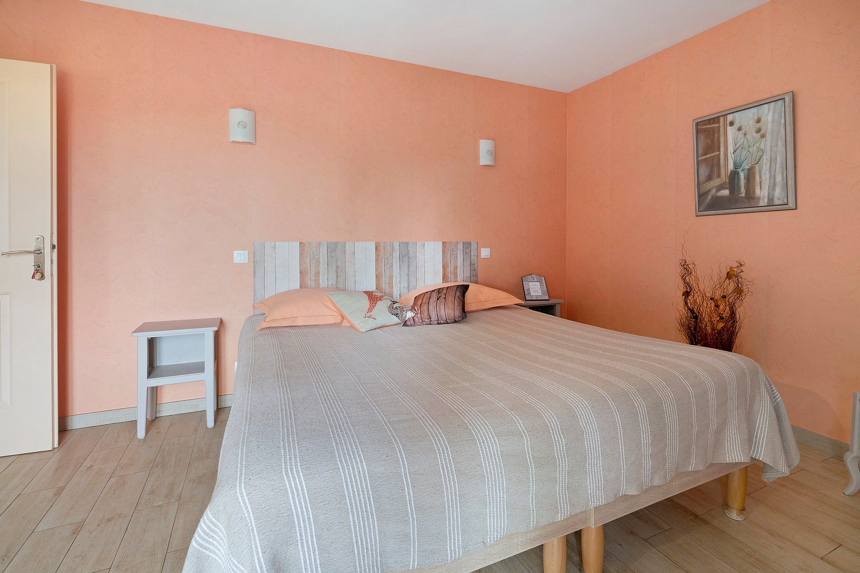 A bedroom with a bed, a nightstand, a small table, and a painting on the wall.