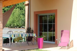 An outdoor patio with a table and chairs, a pink chair, and a large potted plant. - Bed and Breakfast 'Chambre Bon Repos' with Shared Pool, Wi-Fi and Air Conditioning (Saint-Marcel-Paulel)