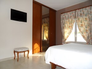 Ein Schlafzimmer mit einem Bett, einem an der Wand montierten Fernseher, einer Sitzbank und einer Tür zu einem anderen Raum.