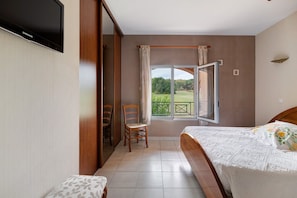 A bedroom with a bed, a chair, a TV, and a window with a view of greenery.