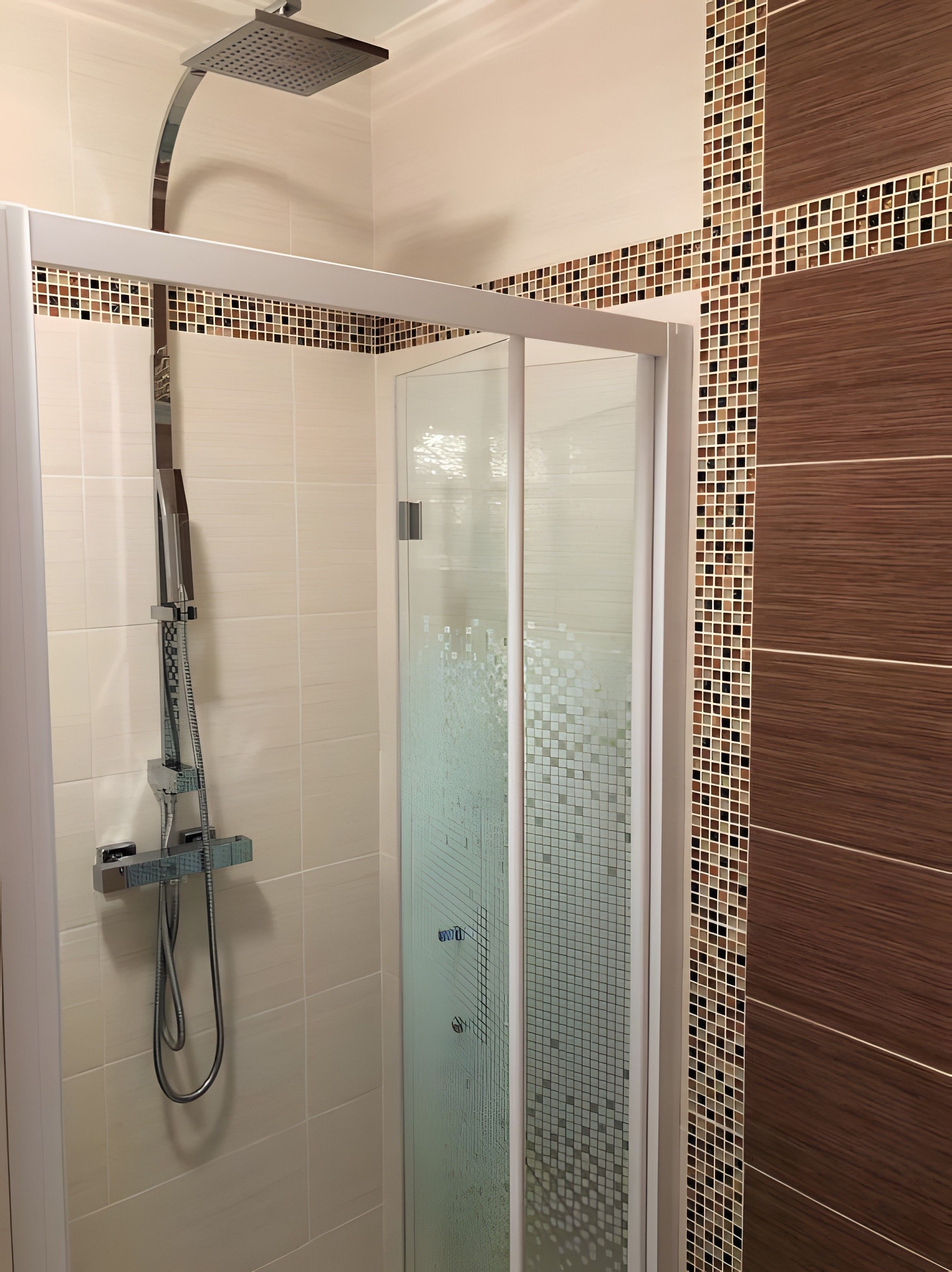 Un espace de douche doté d’une porte en verre, d’un pommeau de douche à main et d’un panneau de commande fixé au mur.