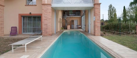 A swimming pool with a sun lounger and a covered area with a spiral staircase.