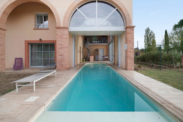 A swimming pool with a sun lounger and a covered area with a spiral staircase.