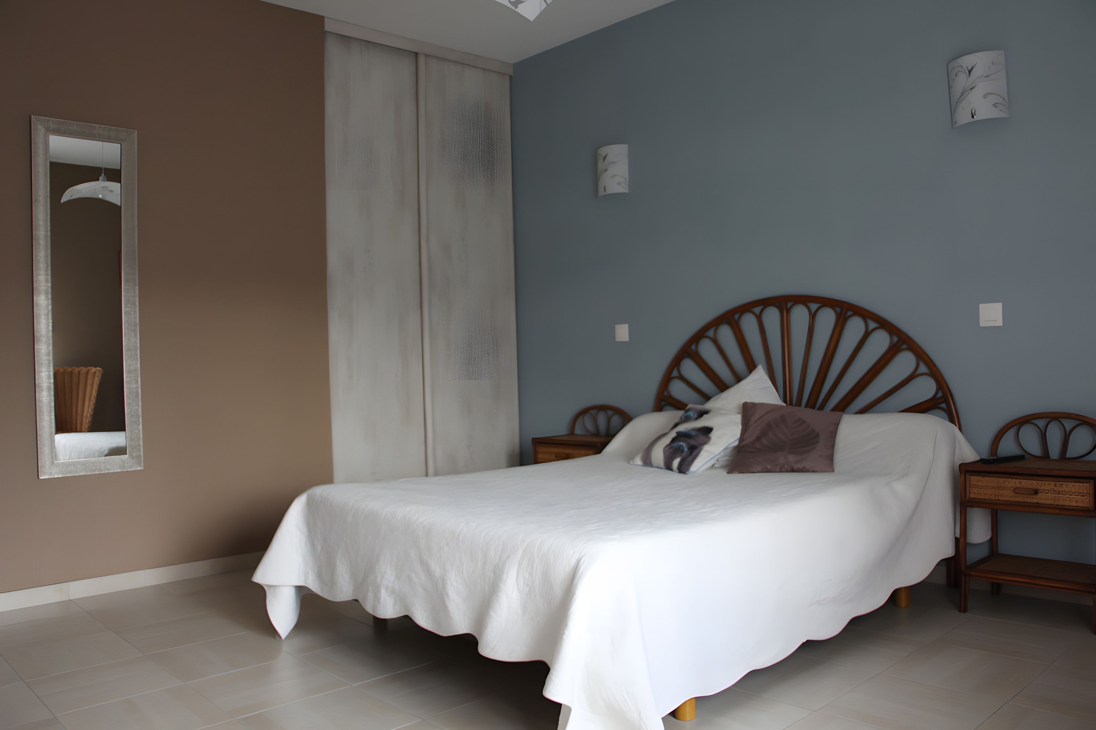 Een slaapkamer met een bed, twee nachtkastjes, een spiegel en een raam met gordijnen.