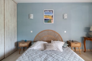 A bedroom with a bed, two bedside tables, a wicker headboard, a poster on the wall, and a lamp on the nightstand.