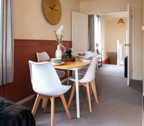 Un coin repas avec une table en bois, des chaises blanches, une horloge murale et une enseigne indiquant « The Beach Suites ».
