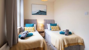 Habitación de hotel con dos camas, un cuadro de una ola, una lámpara y vistas al mar.