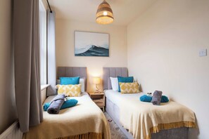 Une chambre d’hôtel avec deux lits, un tableau représentant une vague, une lampe et une vue sur la mer.