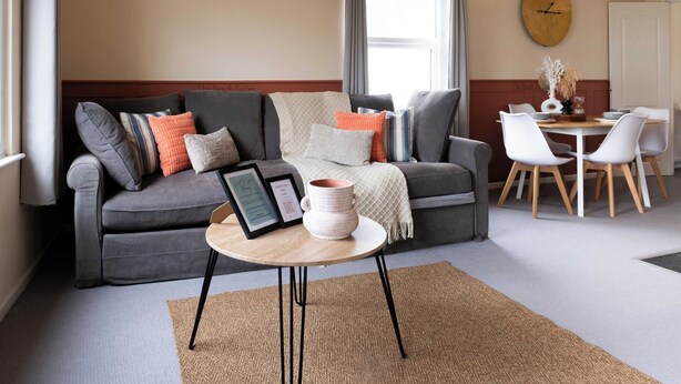 Una sala de estar moderna con un sofá gris, una mesa de centro redonda y una zona de comedor con una mesa y sillas blancas.