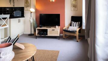 Un espace de vie compact comprenant un téléviseur à écran plat, une table à manger, une chaise et une petite kitchenette.