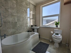 Une salle de bain avec une baignoire, un lavabo, des toilettes et une fenêtre.
