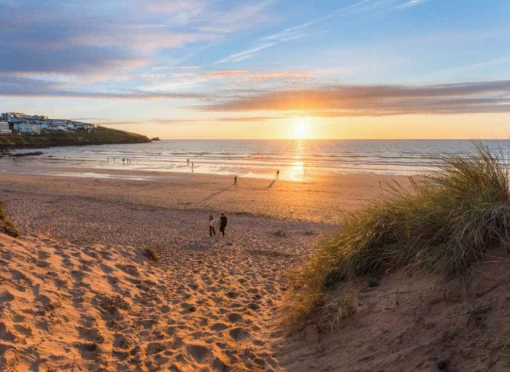 A beach scene with a sunset, sand dunes, and a distant shoreline with buildings.