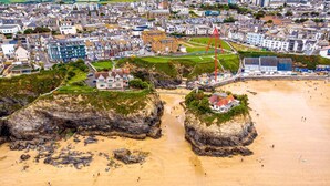 Vista aérea de un pueblo costero con edificios, una playa y afloramientos rocosos.