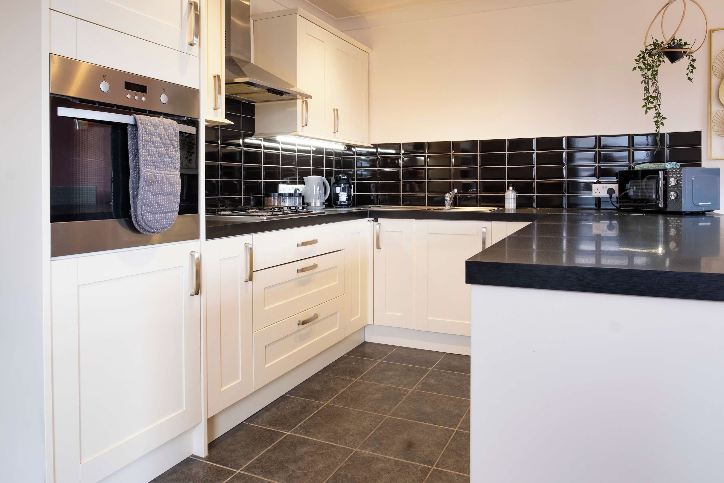 A modern kitchen with white cabinetry, a black countertop, and a black-tiled backsplash.