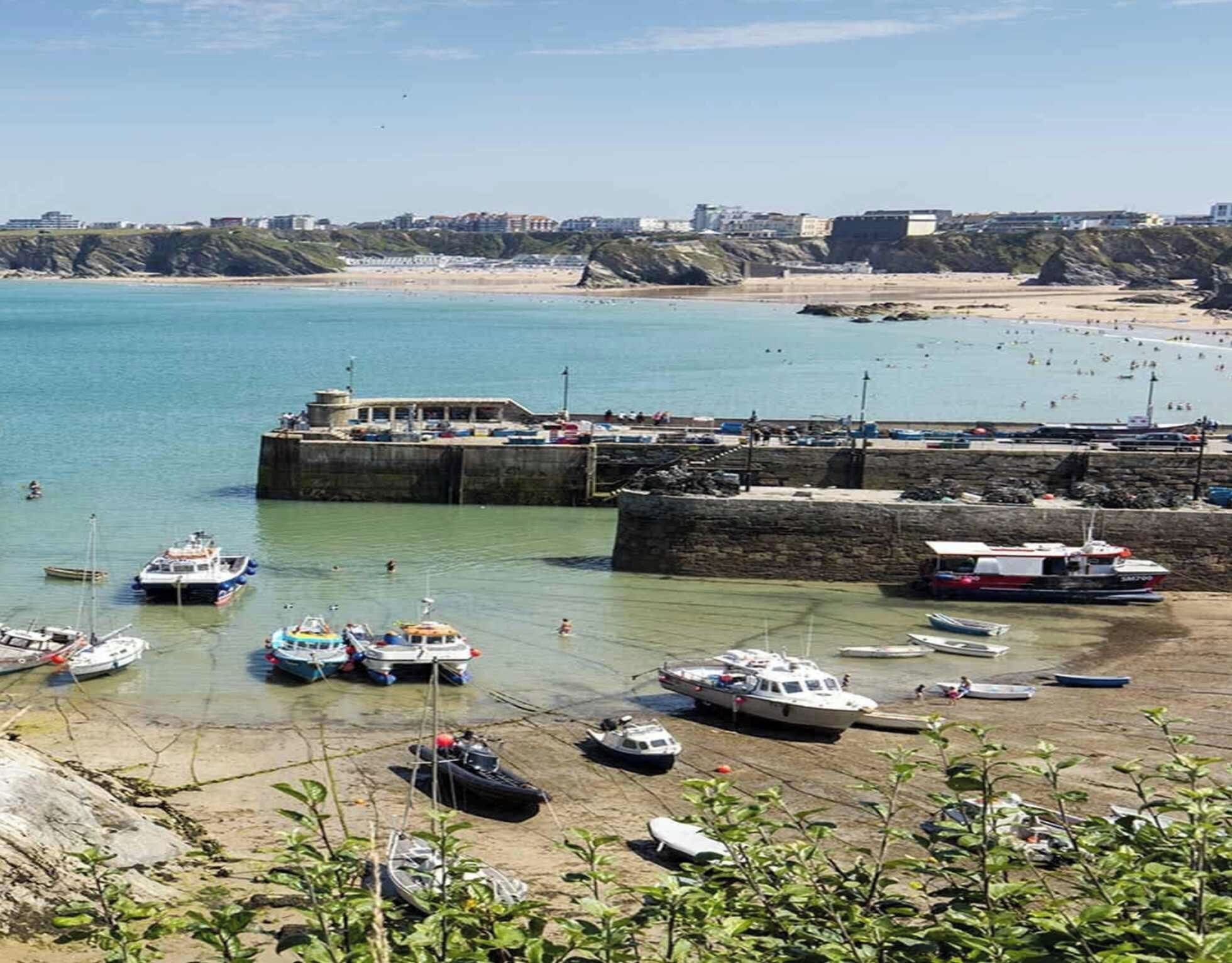 A coastal marina with boats docked, a sandy beach, and a rocky cliff in the background.