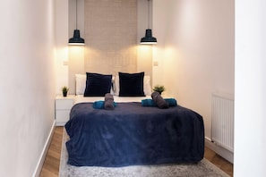Une chambre à coucher comprenant un lit, deux tables de chevet, un radiateur et deux lampes suspendues.