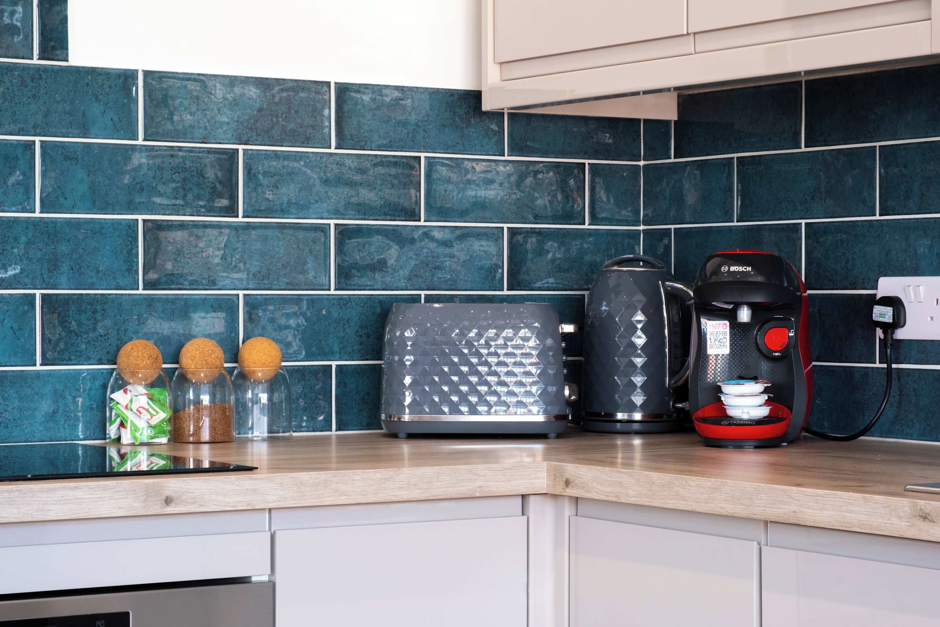 A kitchen with a blue tiled backsplash, a toaster, a coffee maker, and spice jars on the counter.
