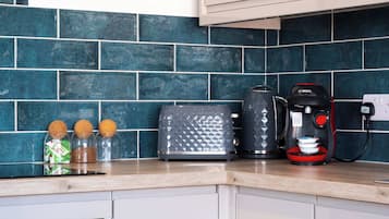 A kitchen with a blue tiled backsplash, a toaster, a coffee maker, and spice jars on the counter.