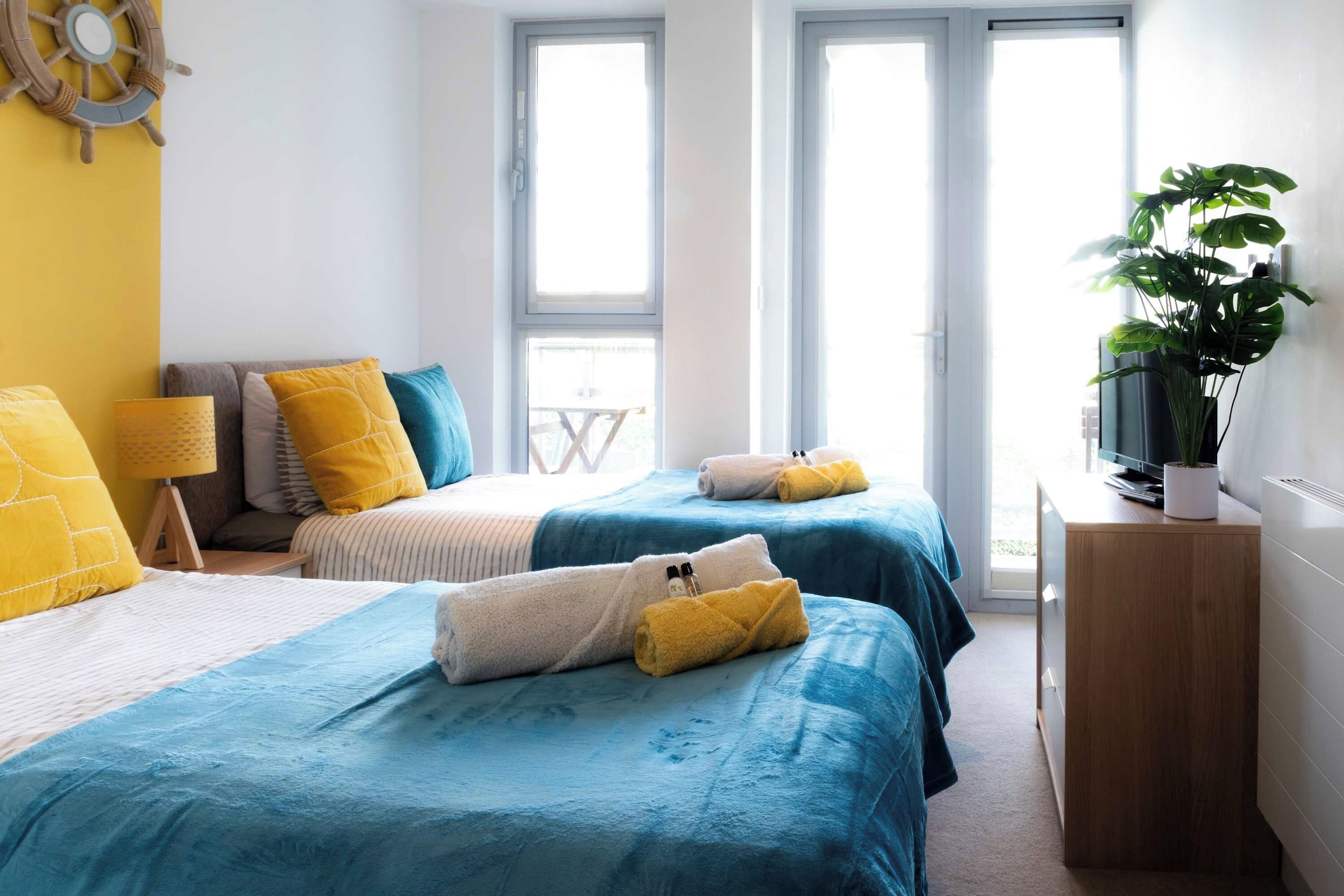 Une chambre d’hôtel avec deux lits, un bureau, une télévision et une plante en pot.