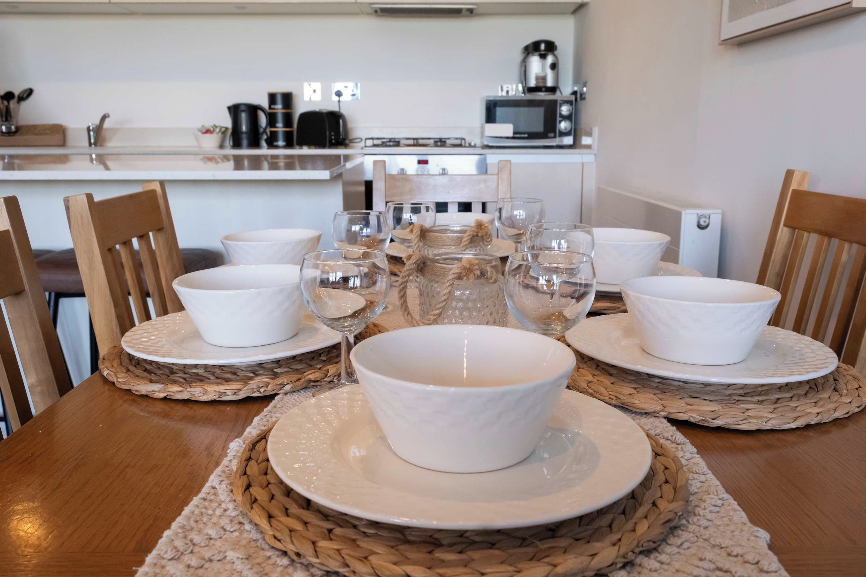 A dining table set with white bowls and glasses, surrounded by woven placemats.