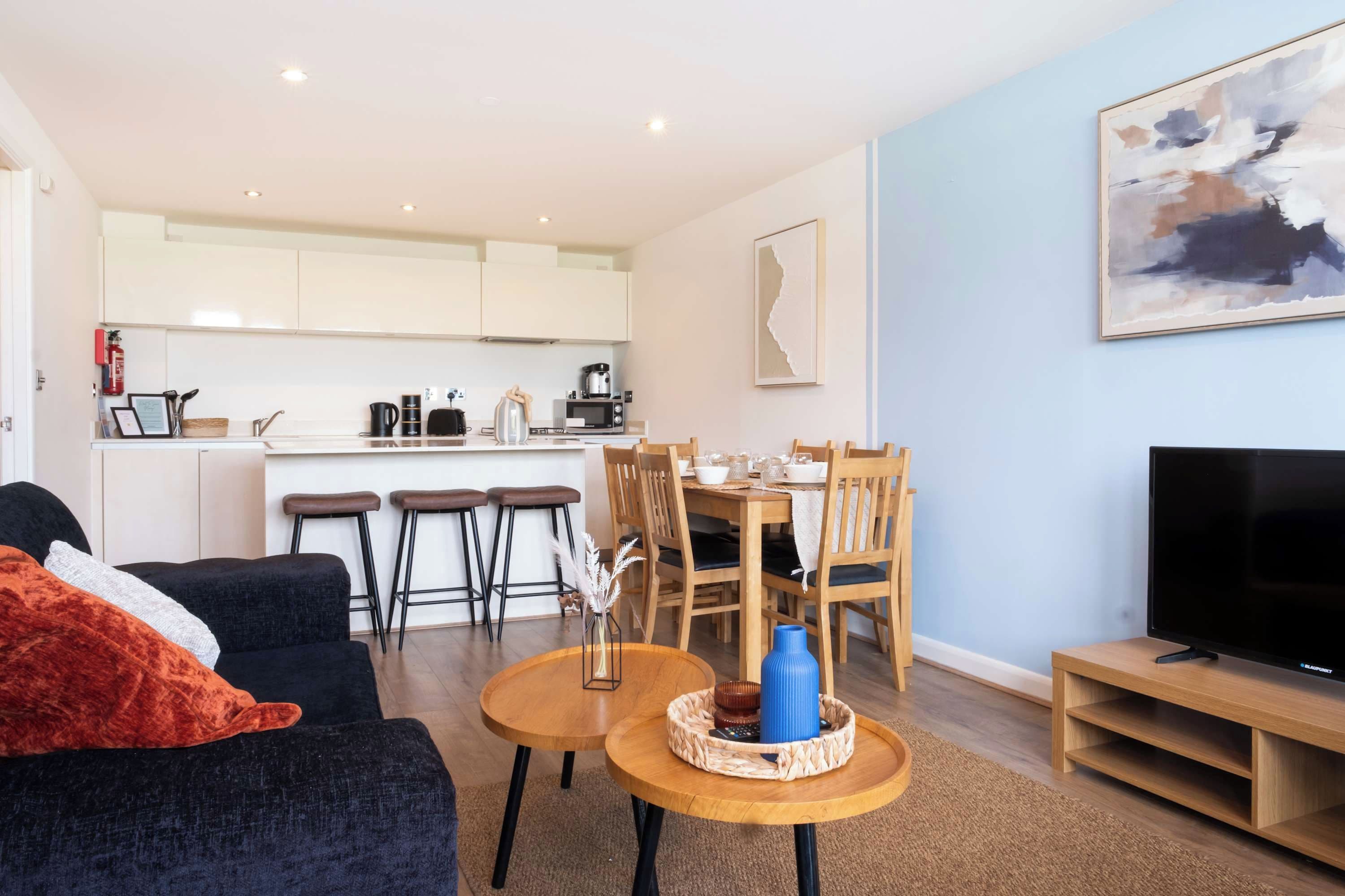 A modern living room with a sofa, a coffee table, a TV, and a dining area with chairs and a table.